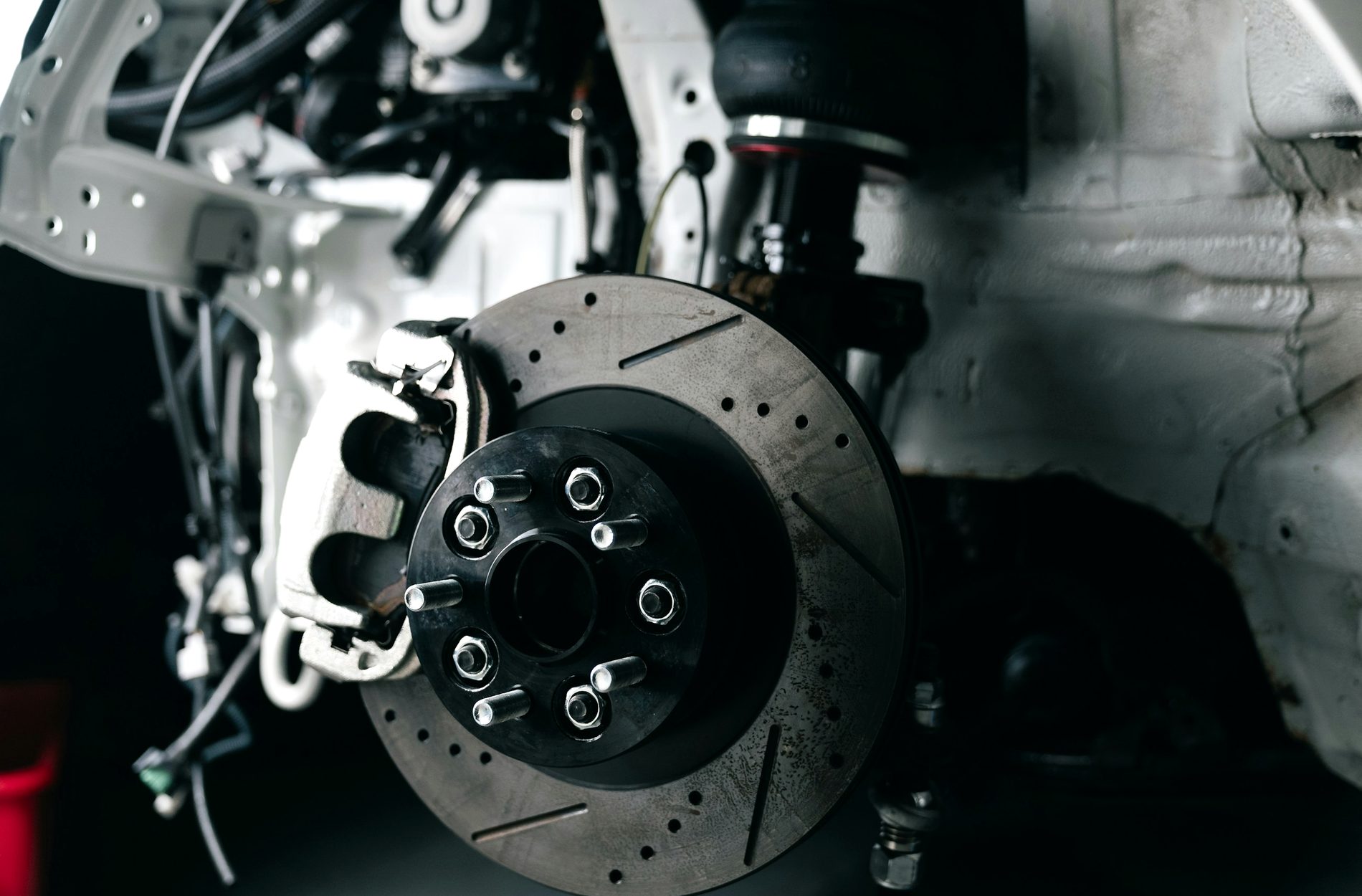 Close-up of a drilled and slotted brake disc and caliper mounted on a car at a workshop